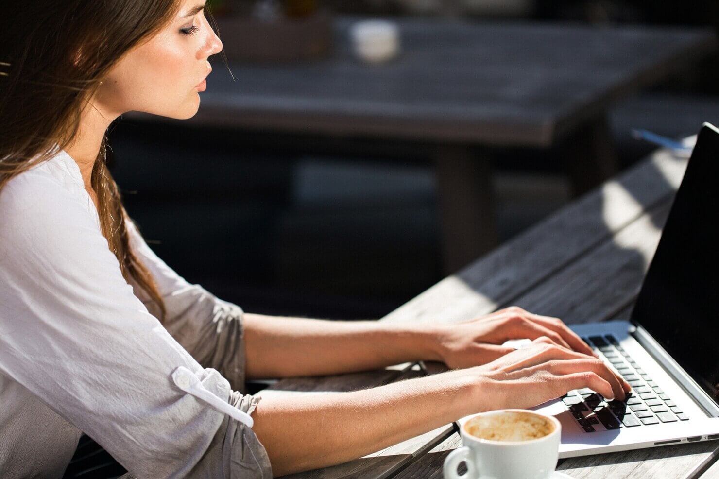 Beautiful brunette works with laptop outside creating a report about how a website audit can uncover revenue opportunities