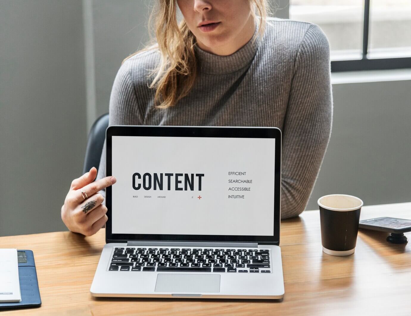 Blond woman pointing at a laptop screen. Various text sizes on screen from WordPress site