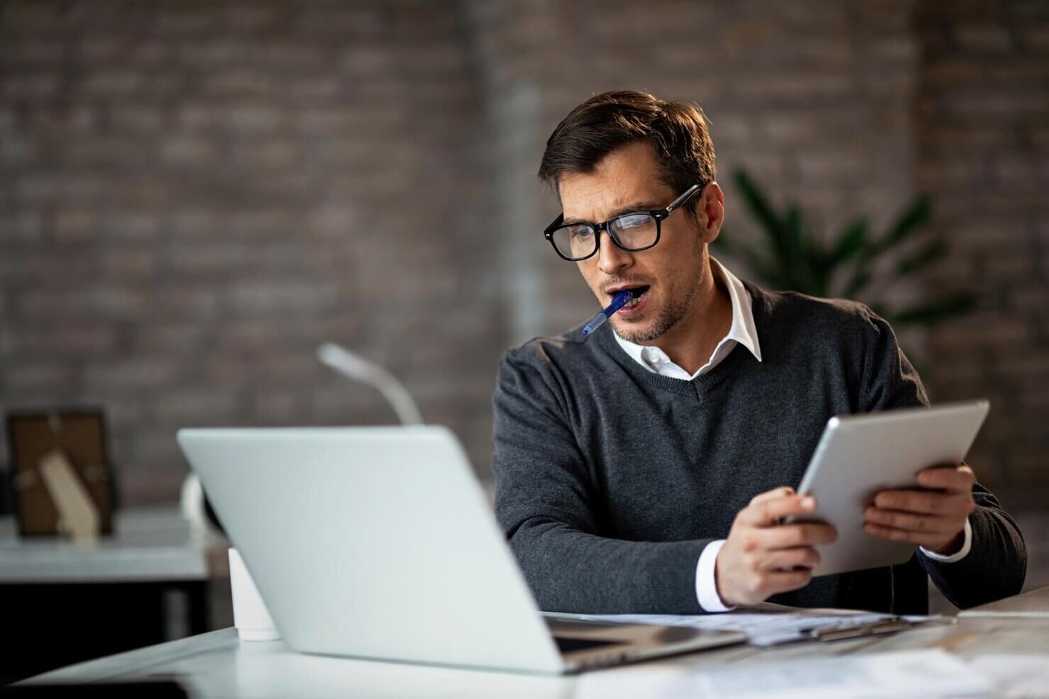 Dedicated businessman using laptop and digital tablet while working in the office. He is documenting his findings from a security audit on a WordPress website