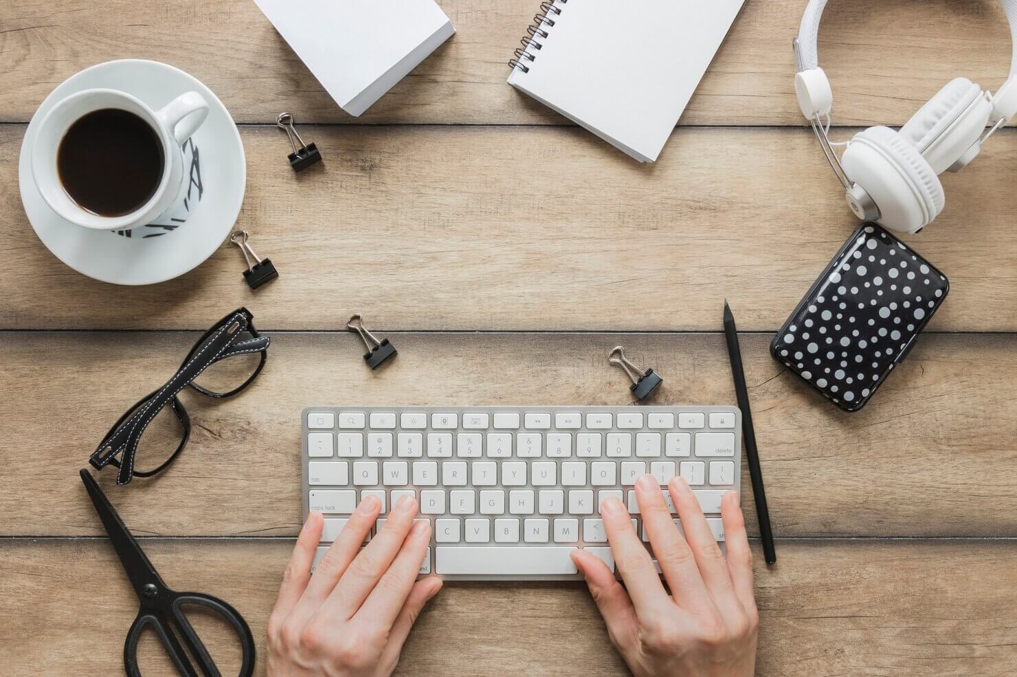 Faceless person typing on keyboard near stationery coffee cup and headphones. Keyboard navigation for website to help person with disabilities