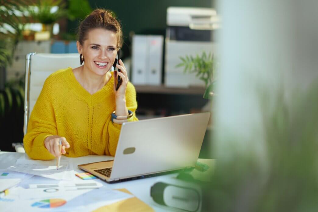 Female talking on the phone about website audit mistakes to avoid performing on her WordPress site at work. Looking at laptop in office