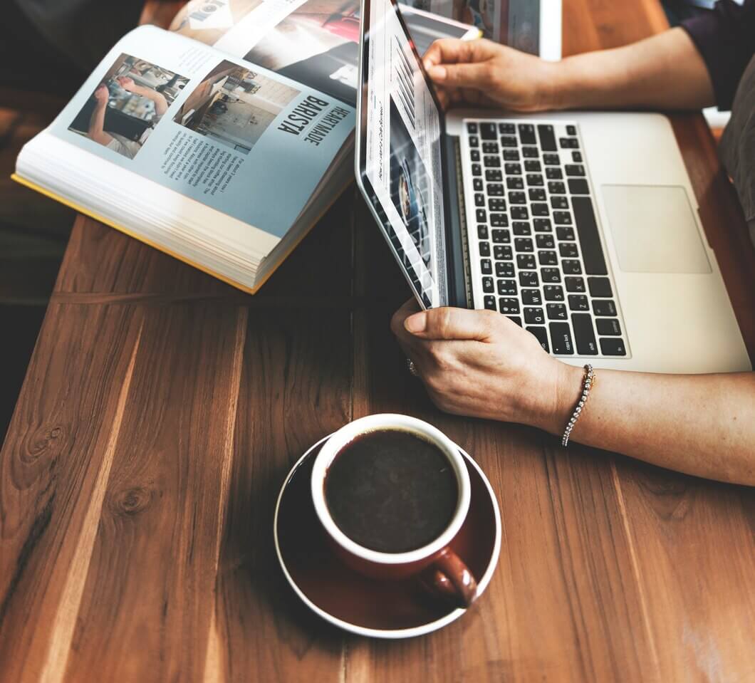 Hands with laptop on wooden table in coffee cafe. Web page has been published.