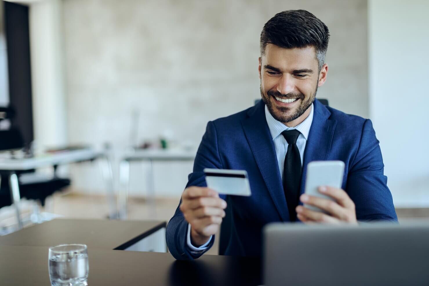 Happy entrepreneur online banking with credit card and mobile phone in the office. Man happy with UX design in financial websites