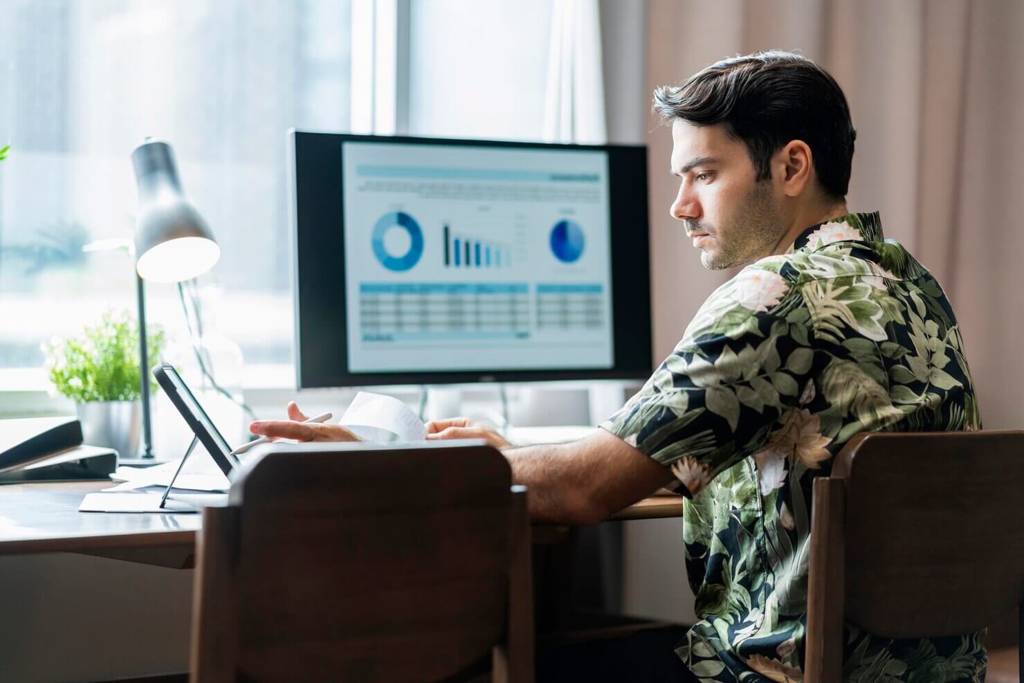 Male developer working with desktop check and analysing business data chart on dinining table at home
