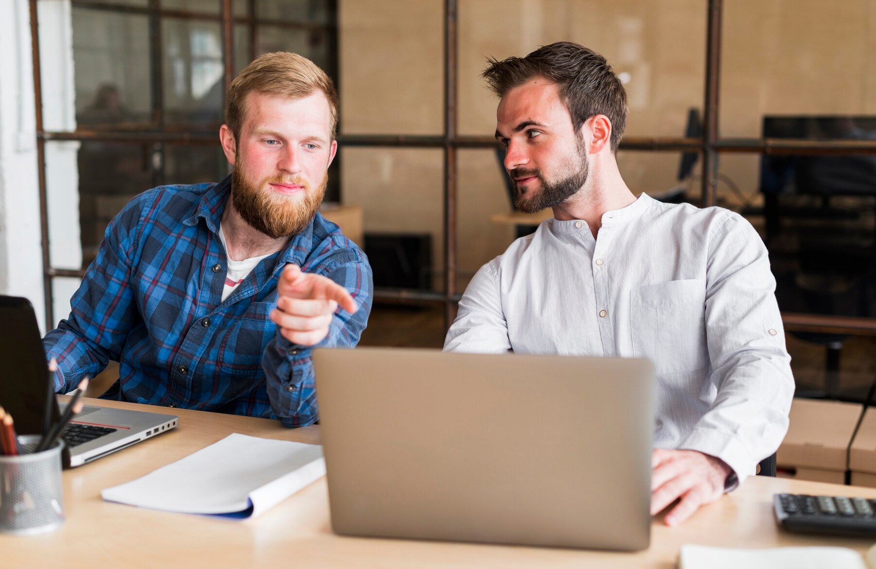 Man pointing finger at his colleague's laptop at workplace. Outsourcing WordPress challenges include poor knowledge transfer
