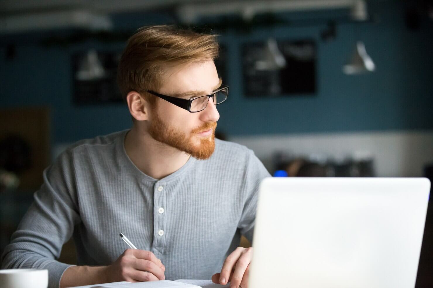 Man thinking of new idea writing notes in cafe. He is writing about the downsides of automated WordPress maintenance