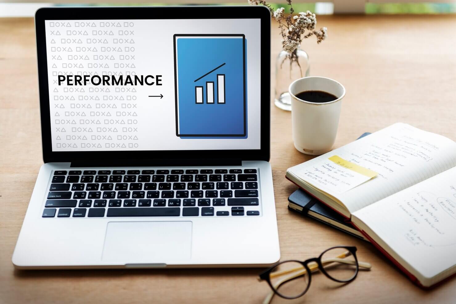 Performance on laptop screen, on desk with notebook and glasses and coffee cup