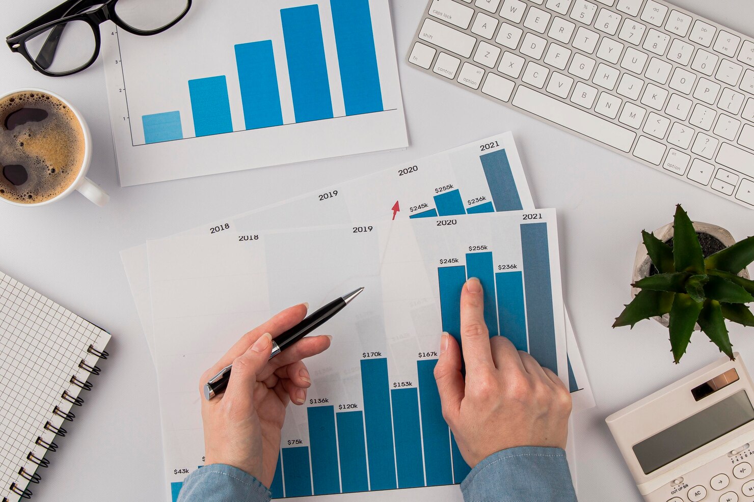 Top view of office desk with growth chart and hands. Many agencies grow their revenue with white-label WordPress development