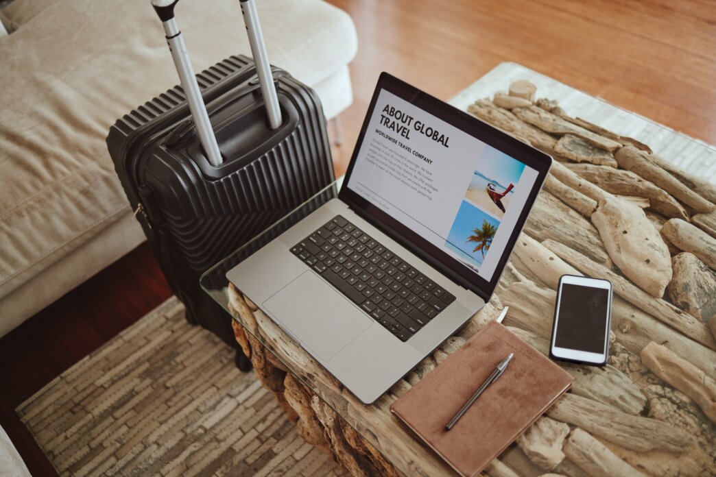 Travel website displayed on laptop on table next to suitcase