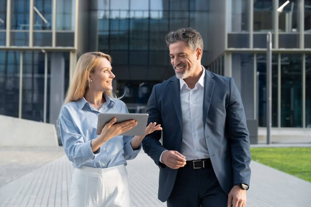 Two business people walking with a tablet in front of office building and discussing whether to choose unlimited support vs hourly woocommerce help