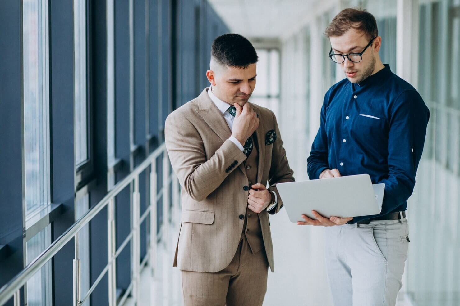 Two male colleagues at the office,standing with laptop trying to identify the right outsourcing wordpress development agencies