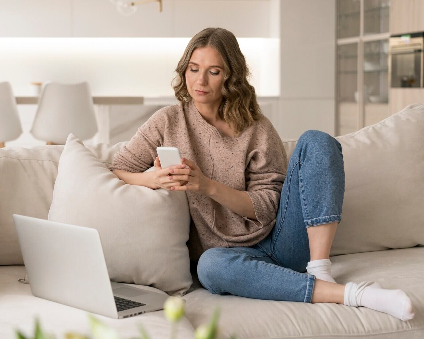 Woman sitting on couch comparing website performance on laptop and mobile phone. Comparing WordPress vs Joomla