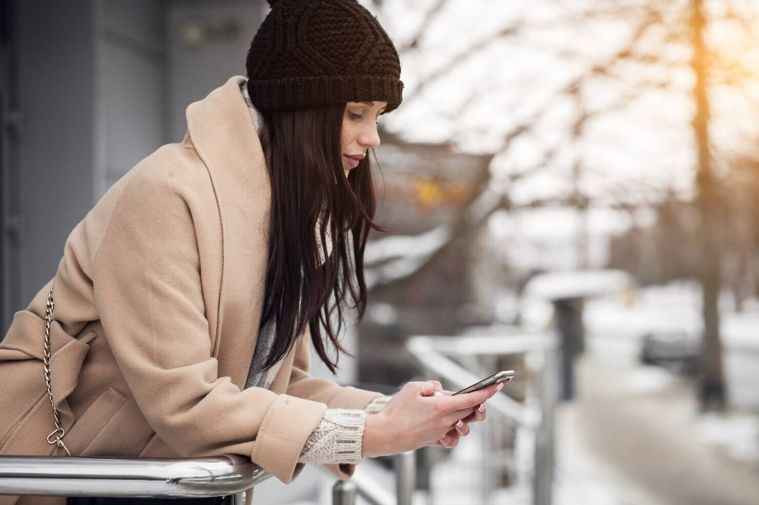 Young female using mobile device in the cold, on a balcony. Mobile sites are more popular than ever